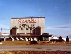 a drive in theatre sign sitting on the side of a road next to a building