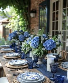 a table set with blue and white plates and vases filled with hydrangeas