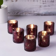 five purple glass candles sitting on top of a white table next to a potted plant