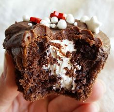 a hand holding a chocolate cupcake with white and red candies on the top