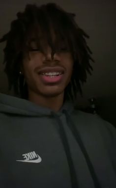 a man with dreadlocks wearing a nike hoodie and smiling at the camera