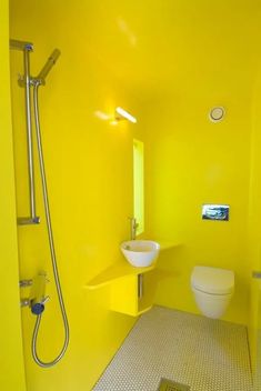 a yellow bathroom with a sink, toilet and shower head mounted to the side of the wall