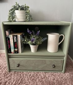 a green shelf with some books and plants on it next to a planter filled with flowers