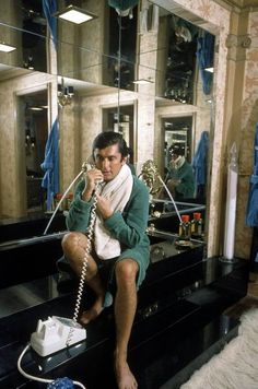 a man sitting in front of a mirror on top of a phone while holding a hair dryer