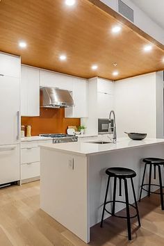 a modern kitchen with white cabinets and wood ceilinging is pictured in this image, there are three stools at the center of the island