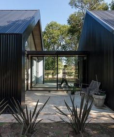 two black buildings sitting next to each other on top of a dirt field with trees in the background