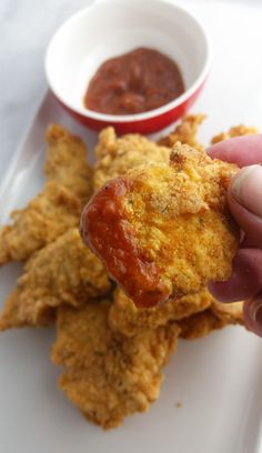 someone is holding up some fried food with sauce in the bowl next to it on a white plate