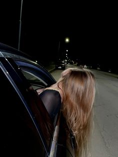 a woman with long hair leaning out the window of a car at night, wearing stockings