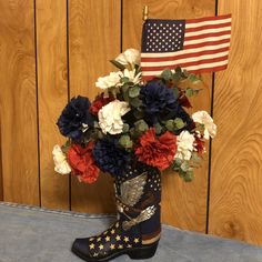 a patriotic flower arrangement in a cowboy boot with an american flag on the wall behind it