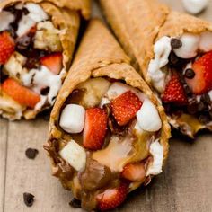 two burritos with strawberries, chocolate and cream on them sitting on a wooden table