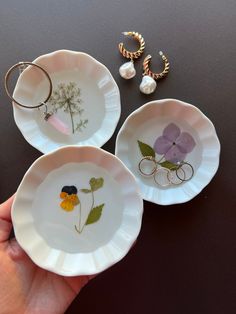 three white dishes with flower designs on them and two gold hoop earrings in the middle