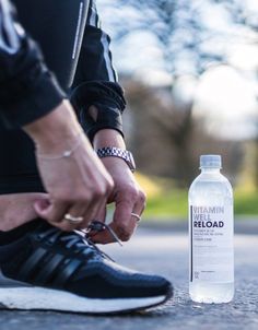 a person tying their shoelaces to a running shoe next to a water bottle