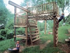 a child playing in the yard under a wooden swing set and tree house with ladders