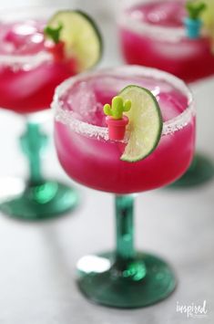 three margarita cocktails with lime slices and garnishes on the rim, sitting on a white surface