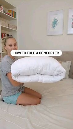 a woman is sitting on her bed and holding a pillow with the words how to fold a comforter