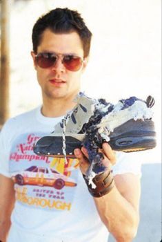 a man wearing sunglasses and holding a pair of shoes