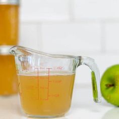 a measuring cup filled with liquid next to an apple