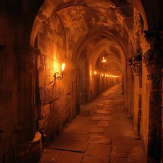 an old tunnel with light at the end and stone flooring on both sides, lit by candles