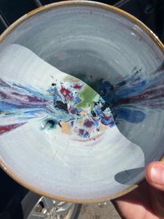 a hand holding a white bowl with multicolored designs on it's rim