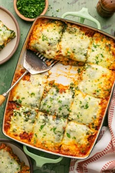 a casserole dish filled with lasagna and spinach on a green table