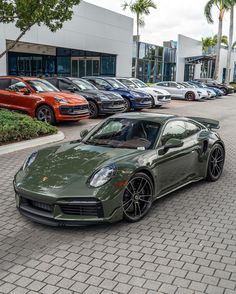 a green sports car parked in front of a building with many other cars behind it