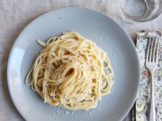 a white plate topped with pasta on top of a table next to a fork and knife