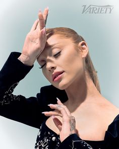 a woman in black dress holding her hand up to her face with both hands on her head