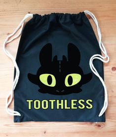 a black bag with yellow eyes and the words toothless on it is sitting on a wooden floor