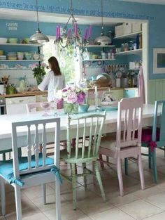 a woman standing at the counter in a blue and white kitchen with chairs around it