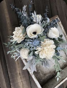 an arrangement of white flowers and greenery in a rustic box on a wooden surface