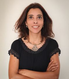 a woman with her arms crossed looking at the camera while wearing a black shirt and gold necklace