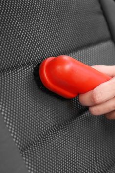 a person is holding a red object in their hand on a black seat cushion with white stitching