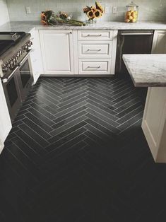 a black and white kitchen with herring tile flooring, stainless steel appliances and marble counter tops