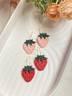 three strawberry shaped earrings sitting on top of a white plate