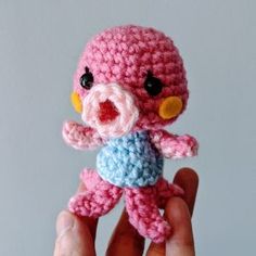 a crocheted pink and blue stuffed animal in someone's hand with white background