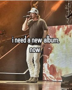 a man standing on top of a stage with a microphone in his hand and the words i need a new album now