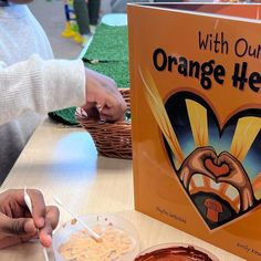 a person sitting at a table in front of an orange heart book and bowl of cereal