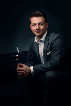 a man in a suit and tie holding a glass of wine on a black background