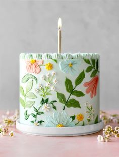 a white cake with flowers on it and a single candle sticking out of the top