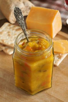 a glass jar filled with food sitting on top of a wooden table next to crackers and cheese