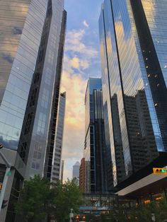 some very tall buildings in the city at sunset or sunrise with clouds reflecting off them