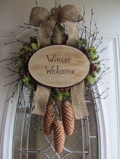 a welcome sign hanging on the front door with two pine cones and evergreens attached to it