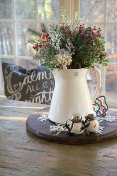 a white pitcher filled with flowers sitting on top of a wooden table next to a window