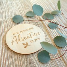 a wooden plaque with the words our greatest adventure is you surrounded by leaves on a table