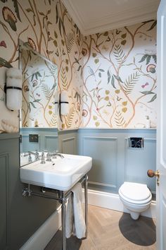 a bathroom with a toilet, sink and wallpapered walls in the background is an open door