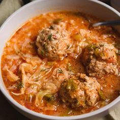 a white bowl filled with meatballs and vegetables in tomato sauce on top of a table