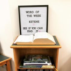 an open book on top of a wooden shelf next to a sign that says word of the week kettene see if you can find it