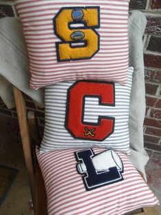 two pillows with letters on them sitting next to each other in front of a brick wall