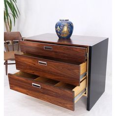 a wooden dresser with two drawers and a blue vase on it's top shelf