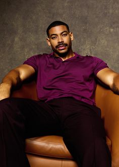 a man sitting on top of a brown leather chair with his arms crossed and legs crossed